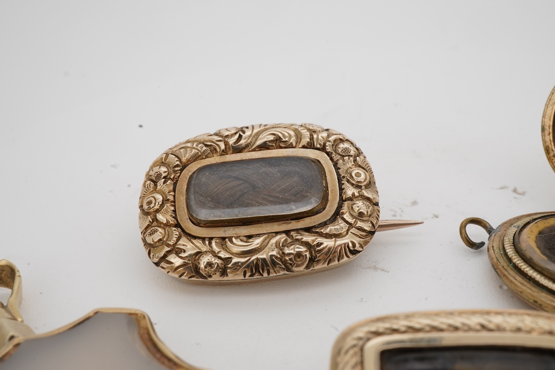 A locket, a watch key and two mourning brooches, the oval locket engraved with foliate details, opening to reveal a glazed panel of hairwork; together with two early 19th century mourning brooches, engraved with flowers